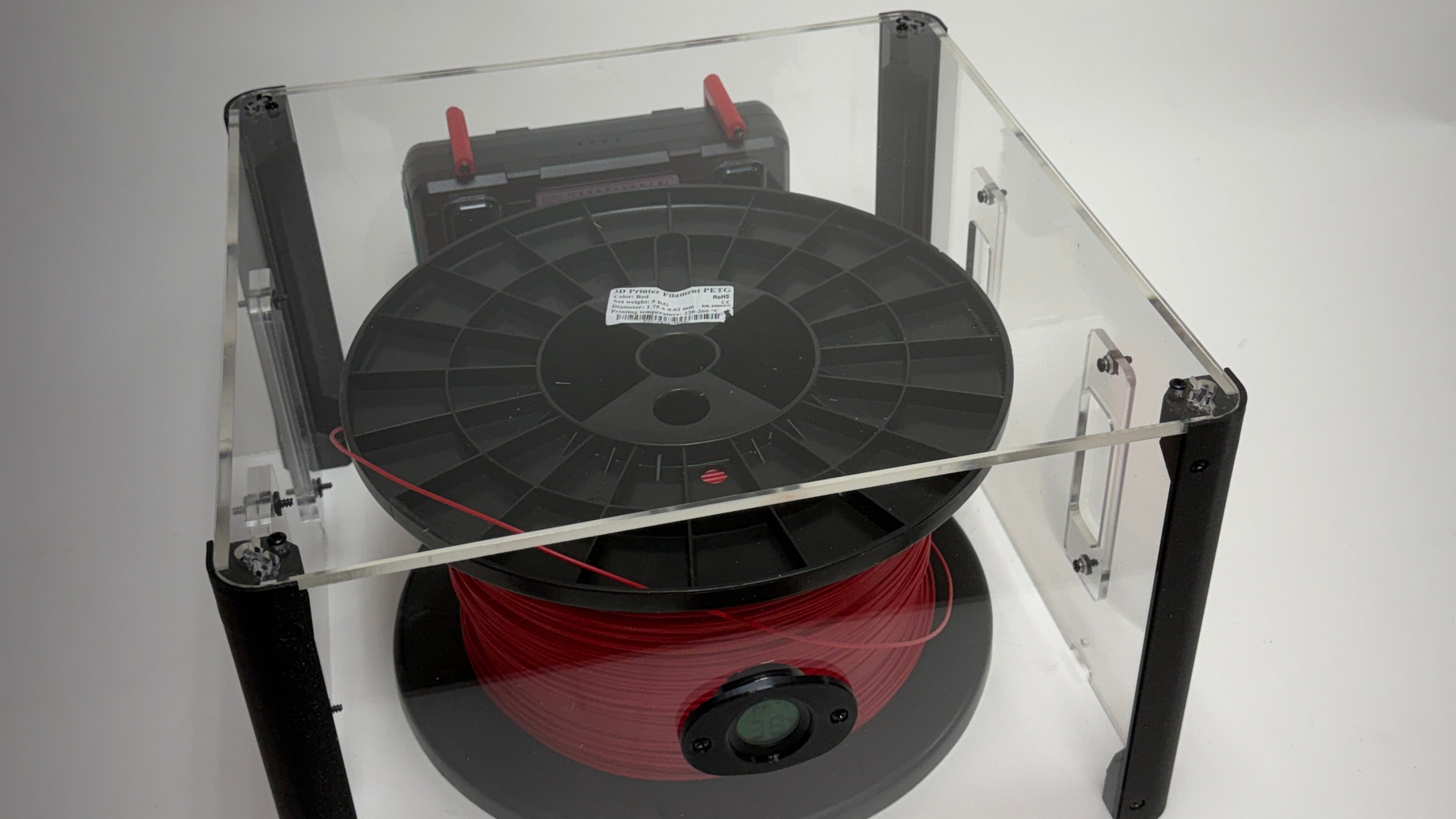 Red spool of thread inside a clear plastic box on a white background